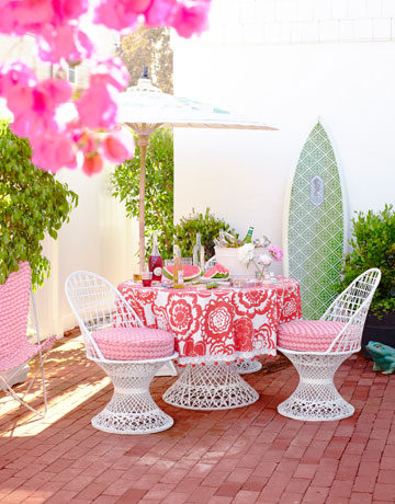 brick outdoor patio with green surfboard, pink table cloth and seat covers, and 1960s furniture